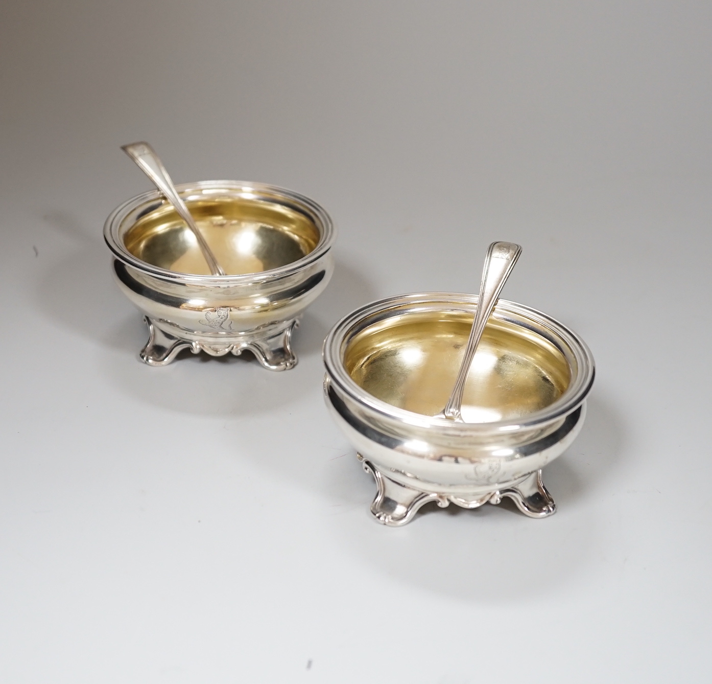 A pair of Victorian circular silver salts, with crests and scroll feet, makers Edward Barnard & Sons, London 1839, 207 grams, and a pair of George IV silver salt spoons, London 1827, 19 grams